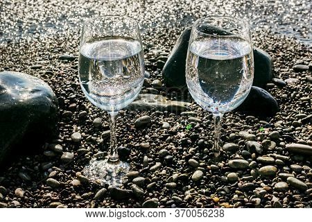Two Pretty Glasses Of Water On Sea Pebbles By Water