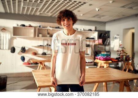 Young Man Smiling At Camera, While Trying On Printed T Shirt, Standing In The Store. Clothes At Cust