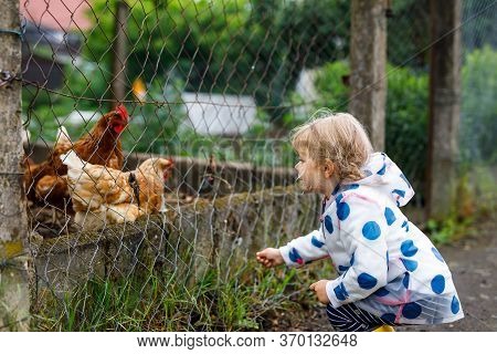 Outdoor Portrait Of Happy Smiling Little Toddler Girl Wearing Rain Jacket On Rainy Cloudy Day Feedin