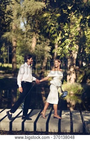 Minimalistic Wedding. Happy Just-married Couple Holding Hands Walking Ourside In Beautiful Park Cele
