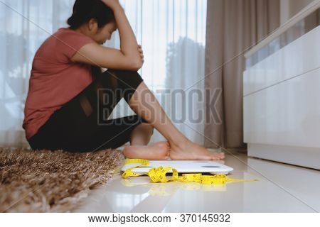 Weight Loss Fail Concept. Scale And Measure Tape With Depressed, Frustrated And Sad Woman Sitting On