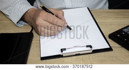 Man's Hand Holds A Pen. On The Table Is A Calculator And Notbook. Accounting, Finance, Banking Conce