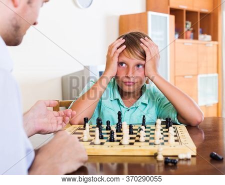 Father And Son Playing Chess At Home, Boy Losing