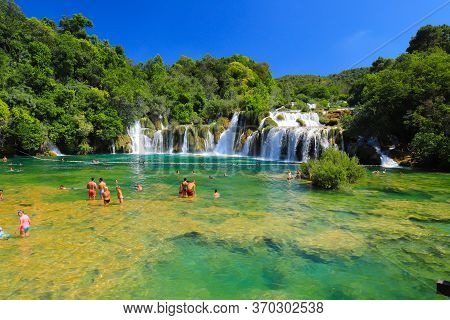 Tourists Swim In The Lake Near Picturesque Cascade Waterfall In The Krka National Park, Croatia In S