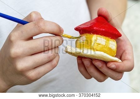 Little Girl Paints The House From Clay Or Salty Dough With Acrylic Paints. Education Concept.