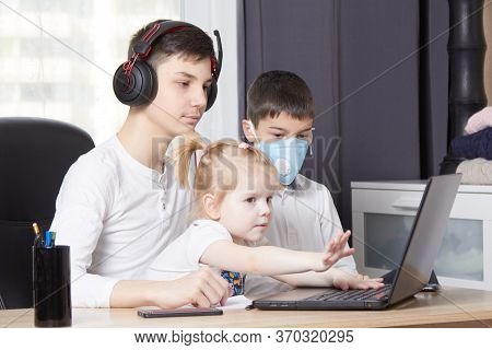 Teenager Looks At A Laptop And Writes Down A Task And Children Interfere With Learning
