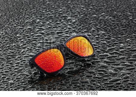 Orange Sunglasses With Water Droplets On Wet Surface