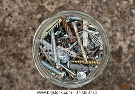 Soft Focus To Assorted Hardware Bolts And Nuts In Glass Jar With Blurry Grunge Stone Background And 