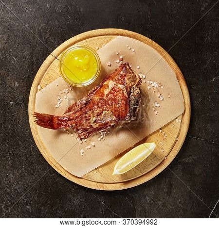 Perch served on piece of parchment and wooden board. Red fish portion on black marble table. Fancy seafood dish. Restaurant main course meal. Exquisite repast. Gourmet food serving