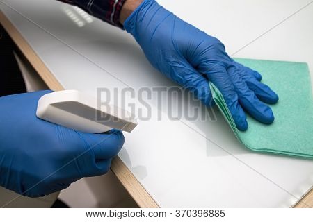 A Man In Blue Protective Gloves Disinfects The Surfaces In The Store Using A Rag And Spray Disinfect