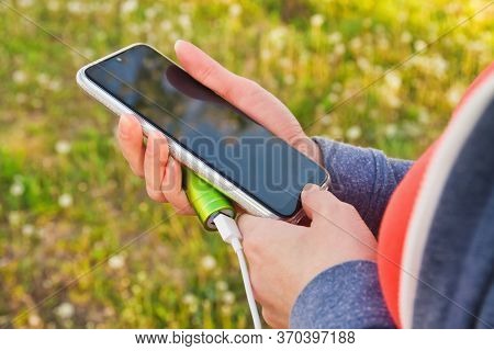 A Girl Uses A Smartphone Outdoors While Charging From An External Power Bank