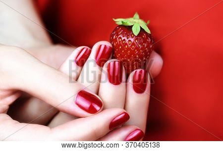 Female Hand With Red Manicure Holding A Strawberry.
