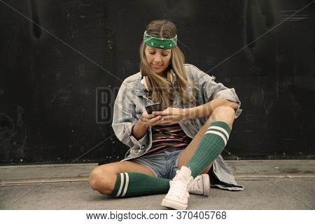 Youthful woman sitting in street texting 