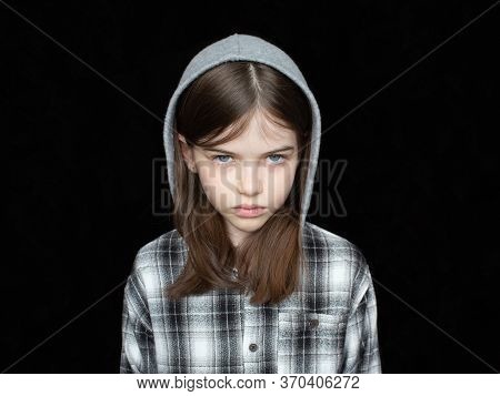 Portrait Of A Little Offended Tearful Girl In A Hoodie On A Black Background