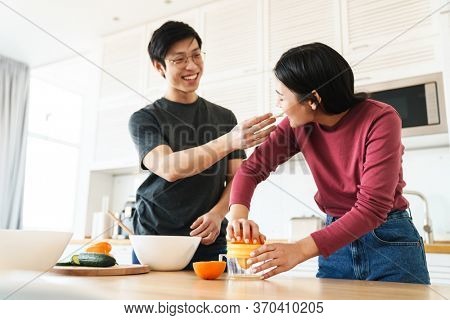 Lovely youg asian couple cooking breakfast together in the kitchen, squeezing oranges for juice