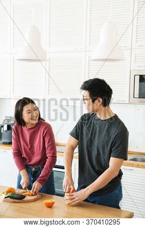Lovely youg asian couple cooking breakfast together in the kitchen, squeezing oranges for juice