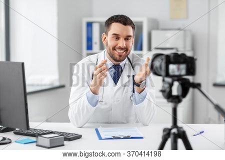 healthcare, medicine and blogging concept - happy smiling male doctor with camera recording video blog at hospital