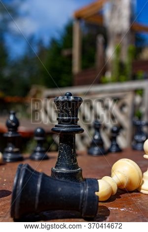 Various Chess Pieces On A Picnic Table With The Focus Centered On A Black Rook, Black Queen, And Whi