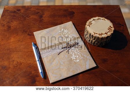 On The Table Is An Open Book Without Text. Near Ballpoint Pen And A Piece Of Round Wood. Place For D