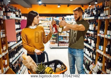 Cheerful couple choosing alcohol in supermarke