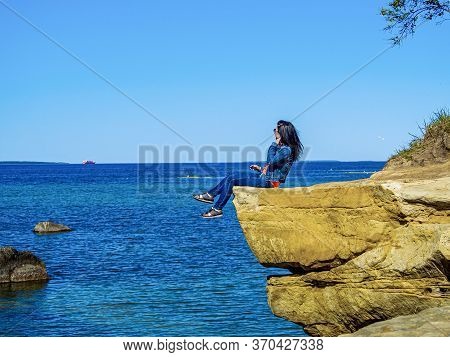 Beautiful Young Girl Siting On A Mountain Pick. Cliff On The Coast Of The Baltic Sea. Sunset Time An