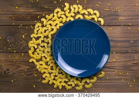Pene Lisce Pasta In The Shape Of A Month Around A Blue Plate On Dark Wooden Background. Top Views.