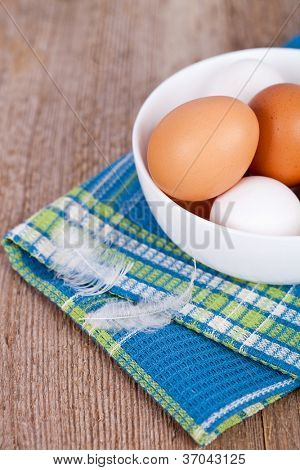 oeufs dans un bol, serviette et plumes sur la table en bois rustique