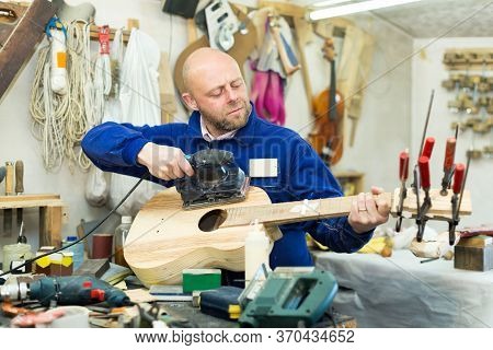 Portrait Concentrated Adult Male Craftsman Working With Unfinished Guitar Indoors