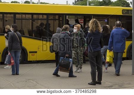 People Leave The Yellow Bus At A Public Transport Stop, And Medical Protective Masks On Passengers. 