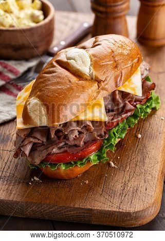 Roast Beef Submarine Sandwich With Cheese, Tomato And Lettuce On A Wooden Cutting Board