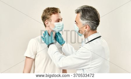 Sore Throat. Professional Mature Doctor Checking Thyroid Glands Of Young Male Patient. Doctor And Pa