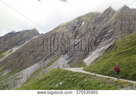 An Alpinist On A Road Surrounded By Rocky Mountains In The Fog In Austrian Alps Near The Grossglockn
