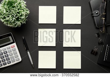 Top view of modern black office desk with calc, notebook, pen, blank sticker and a lot of things. Flat lay table layout. Copy space for text.