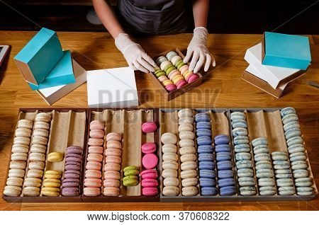 Female hands in gloves packs traditional french dessert macaroon in paper boxes for delievery