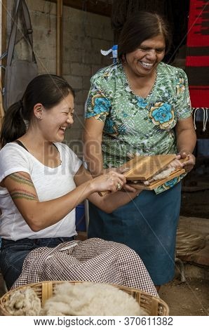 Oaxaca, Mexico - 2019-11-30 - Young Woman Tourist Tries To Card Wool Under The Instruction Of A Mast