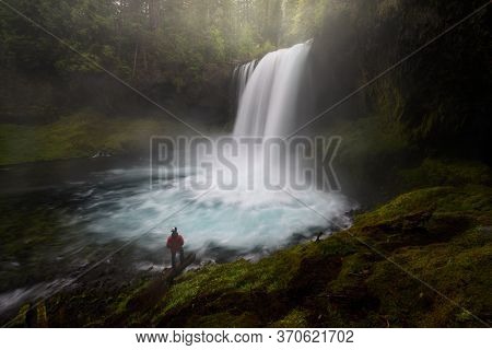 Koosah Falls With Glacial Maelt Blue Color Water. A Man Standing In The Scene For The Sense Of Scale
