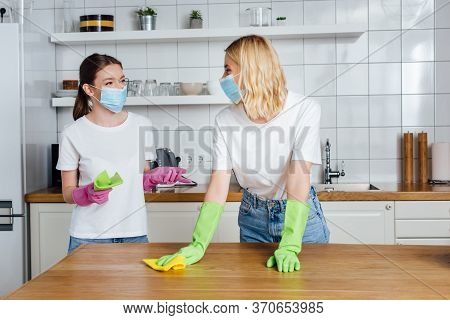 In Medical Masks And Latex Gloves Holding Rags While Doing Housework