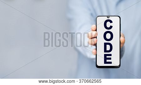 Man's Hand In A Blue Shirt Holding Smartphone With Text Code On A Blue Background