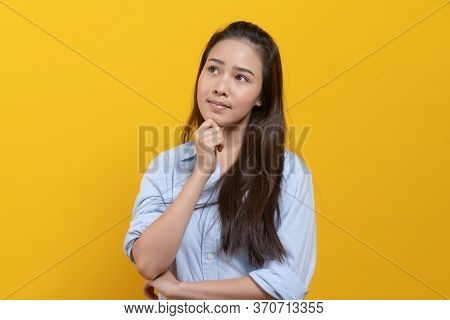 Cute Asian Woman In Casual Dress Thinking And Imagination Isolated On Yellow Background
