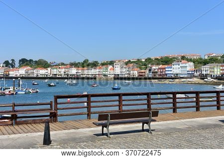 Mugardos, Spain. May 30, 2020. Fishing Village With Wooden Boardwalk, Bench And Boats With Blue Sky.