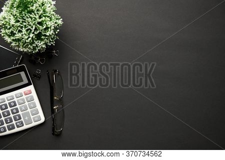 Top view of modern black office desk with calc, notebook, pen and a lot of things. Flat lay table layout. Copy space for text.