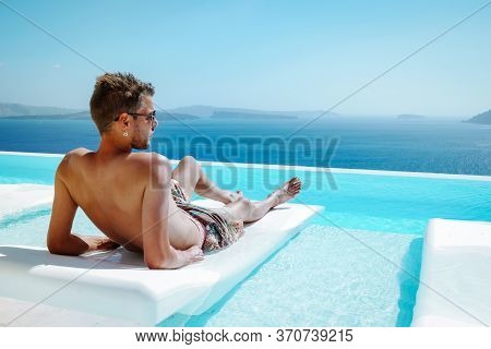 Santorini Greece Oia, Young Men In Swim Short Relaxing In The Pool Looking Out Over The Caldera Of S