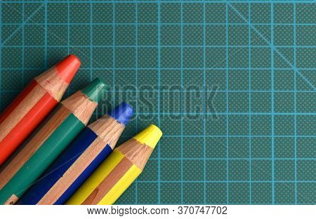 Rgby (red, Green, Blue, Yellow) Colored Pencils Emerging From The Corner Of A Dark Green Cutting Mat