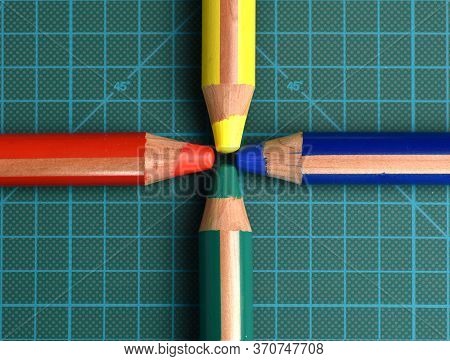 Rgby (red, Green, Blue, Yellow) Colored Pencils Converging Towards The Center Of A Dark Green Cuttin