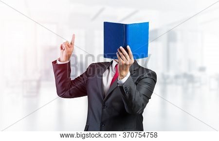 Businessman Covered His Face With Book And Finger Pointing Up. Portrait Of Man In Business Suit Stan