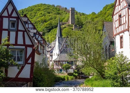 The Village Monreal With River Elz, Half-timbered Houses And Castle Loewenburg In The Background