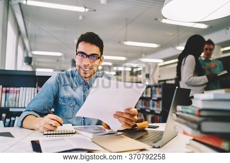 Smiling Male Student Making Coursework Project In College Library