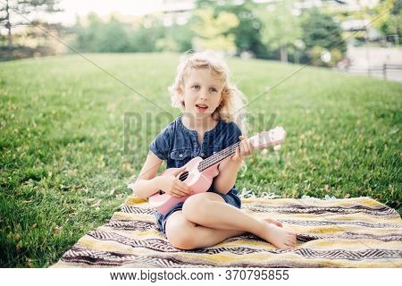 Cute Adorable Blonde Girl Playing Pink Guitar Toy Outdoor. Child Playing Music And Singing Song In P