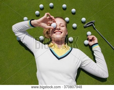 Young female golfer lying on green holding ball in front of eye view from above