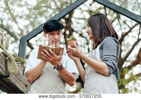 Women Hold Cactus And A Man Writing Note In A Book. Love Couple Enjoy Hobby With Darden Cactus.